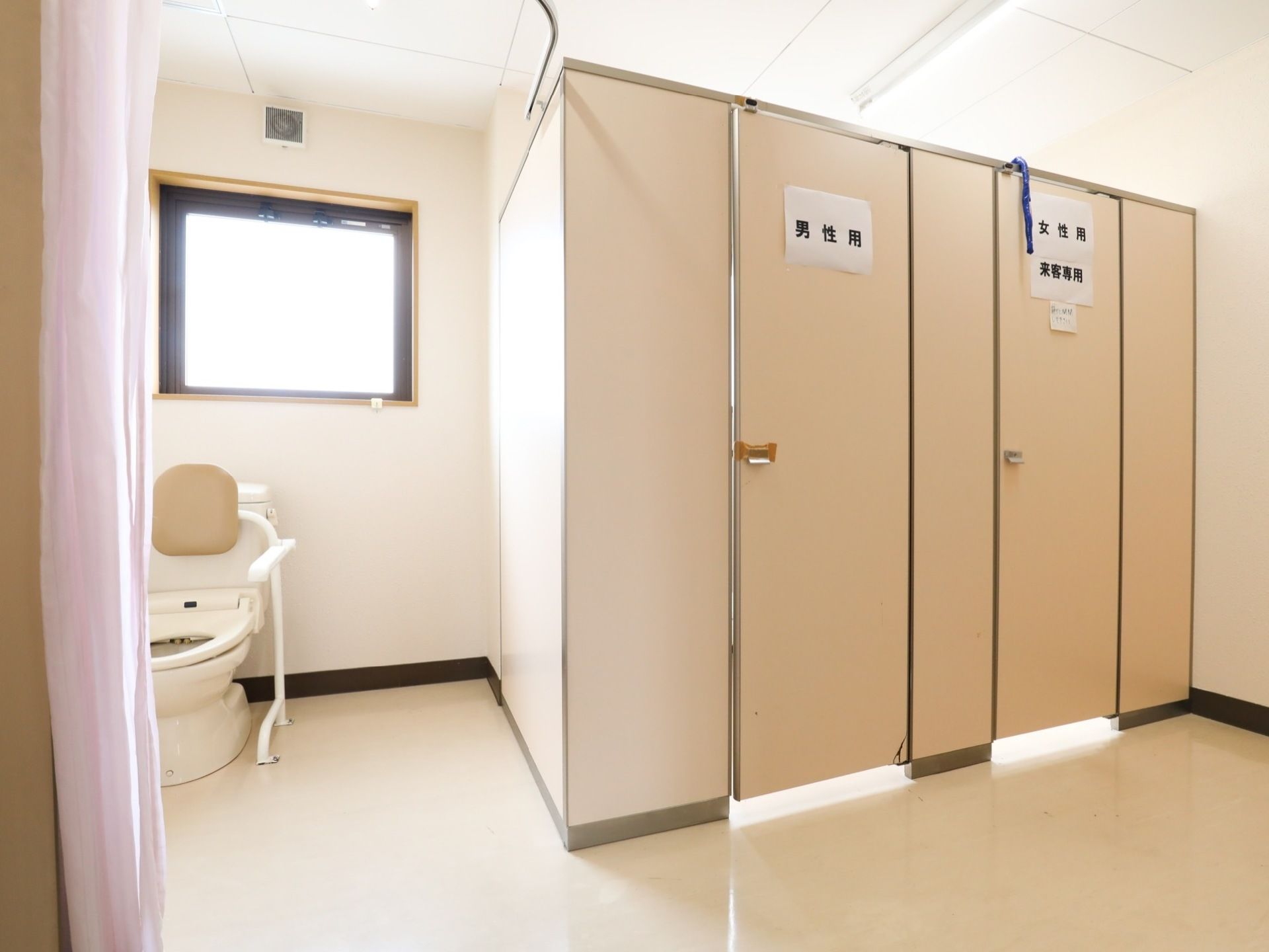 共有トイレには、男性用と表示された個室扉と、女性用来客様用と書かれた個室扉が並んでいる。その他、窓側には介護用便座も設置されている。
