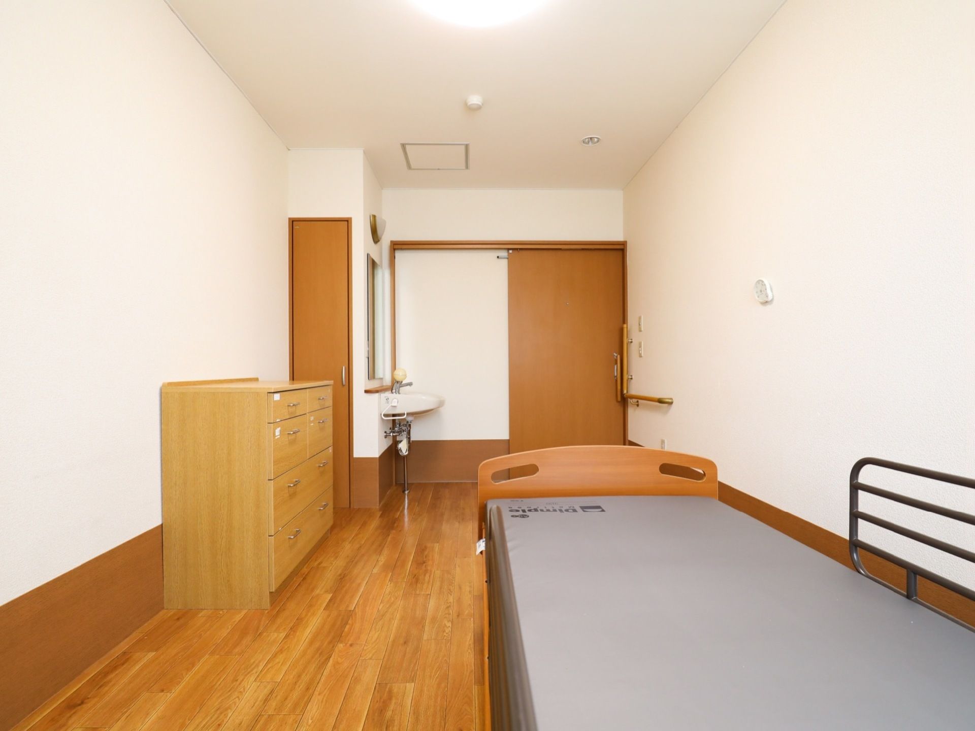 木のぬくもりと清潔感が感じられる室内である。ドアは引き戸で段差がなく、収納タンス、ベッド、洗面台が備えつけられている。