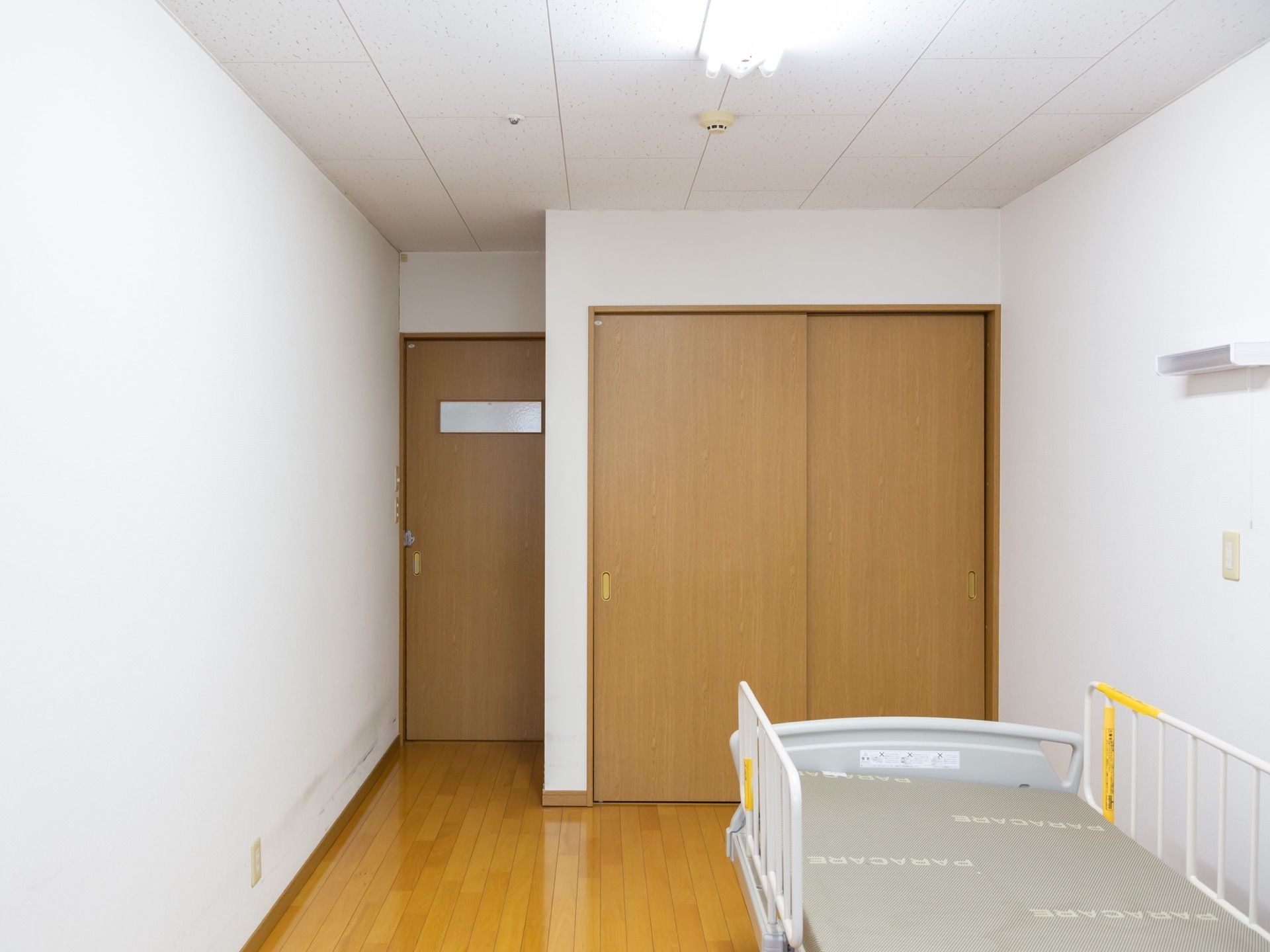 居室には収納スペースが確保されている。収納の前には介護用ベッドが置かれている。床がフローリングになっている。