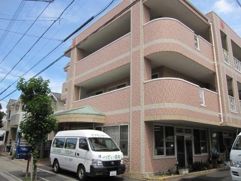 施設は鮮やかな色合いをした３階建ての建物である。入居者様の居室が並ぶ２階以上の階層には一続きのベランダが整備されている。
