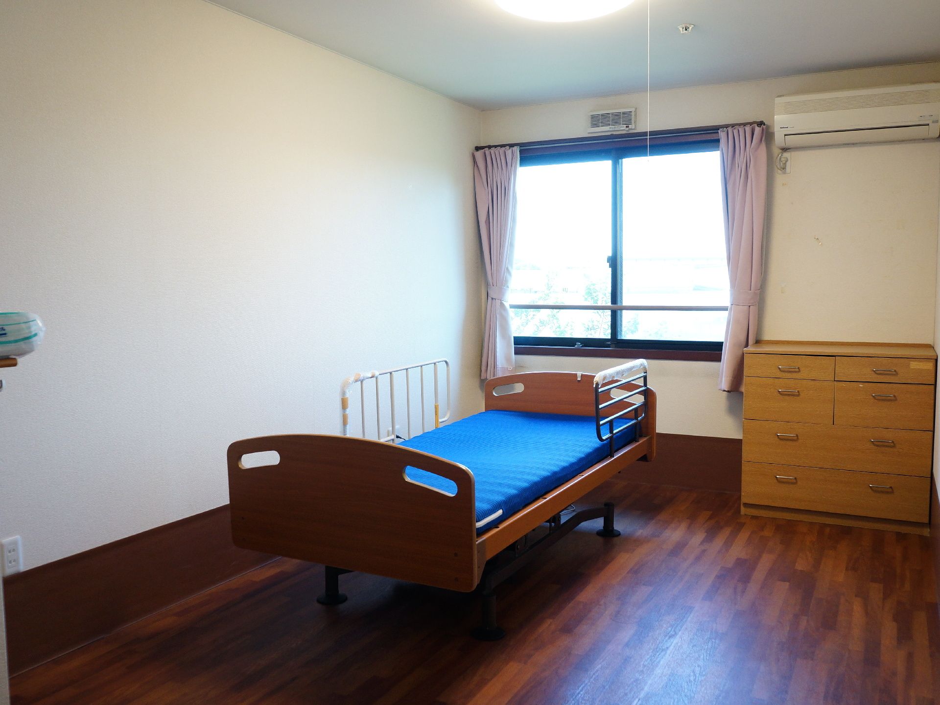 広々とした居室には、介護用ベッドが置かれている。また室内にはローチェストがあり、壁には空調設備を完備している。