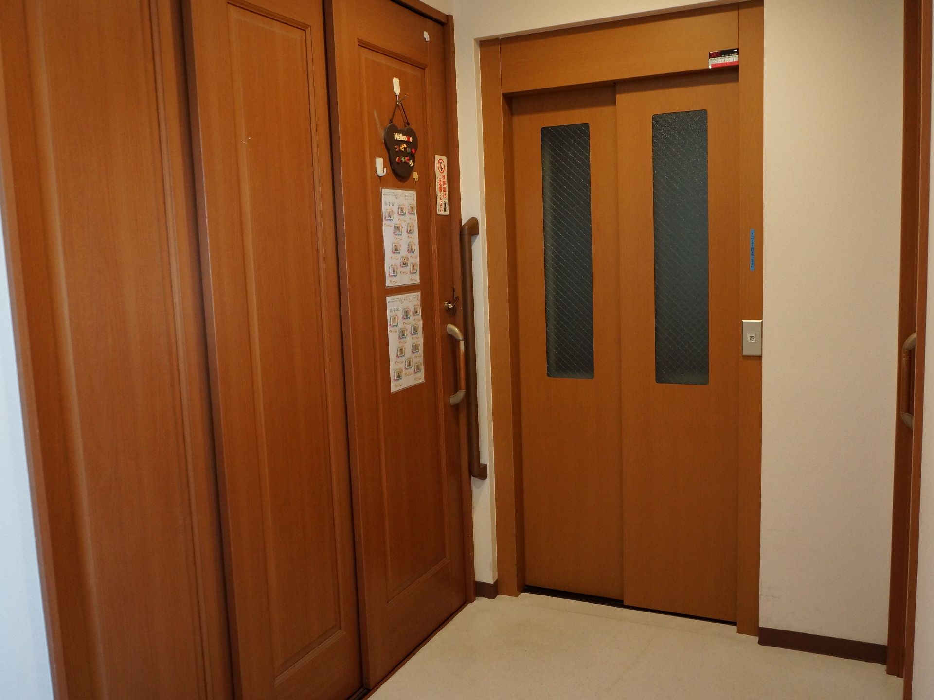 木目調のエレベータードアで、落ち着いた雰囲気である。隣の部屋のドアは引き戸式である。壁には手すりが取りつけられている。