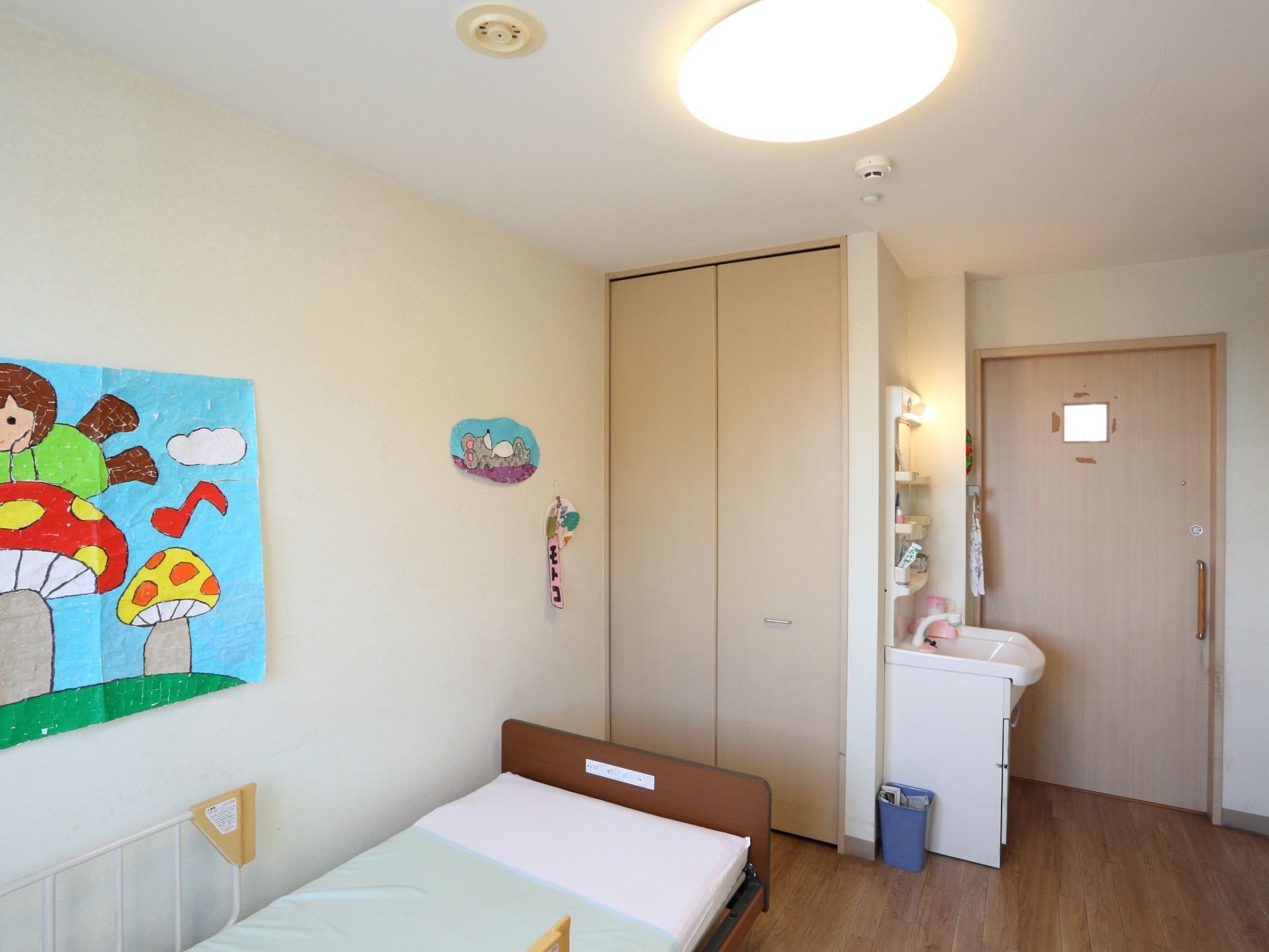 居室にベッドや洗面台、ゴミ箱がある。居室入り口には横開きのドアがついている。居室入り口の幅が広く、出入りしやすい。