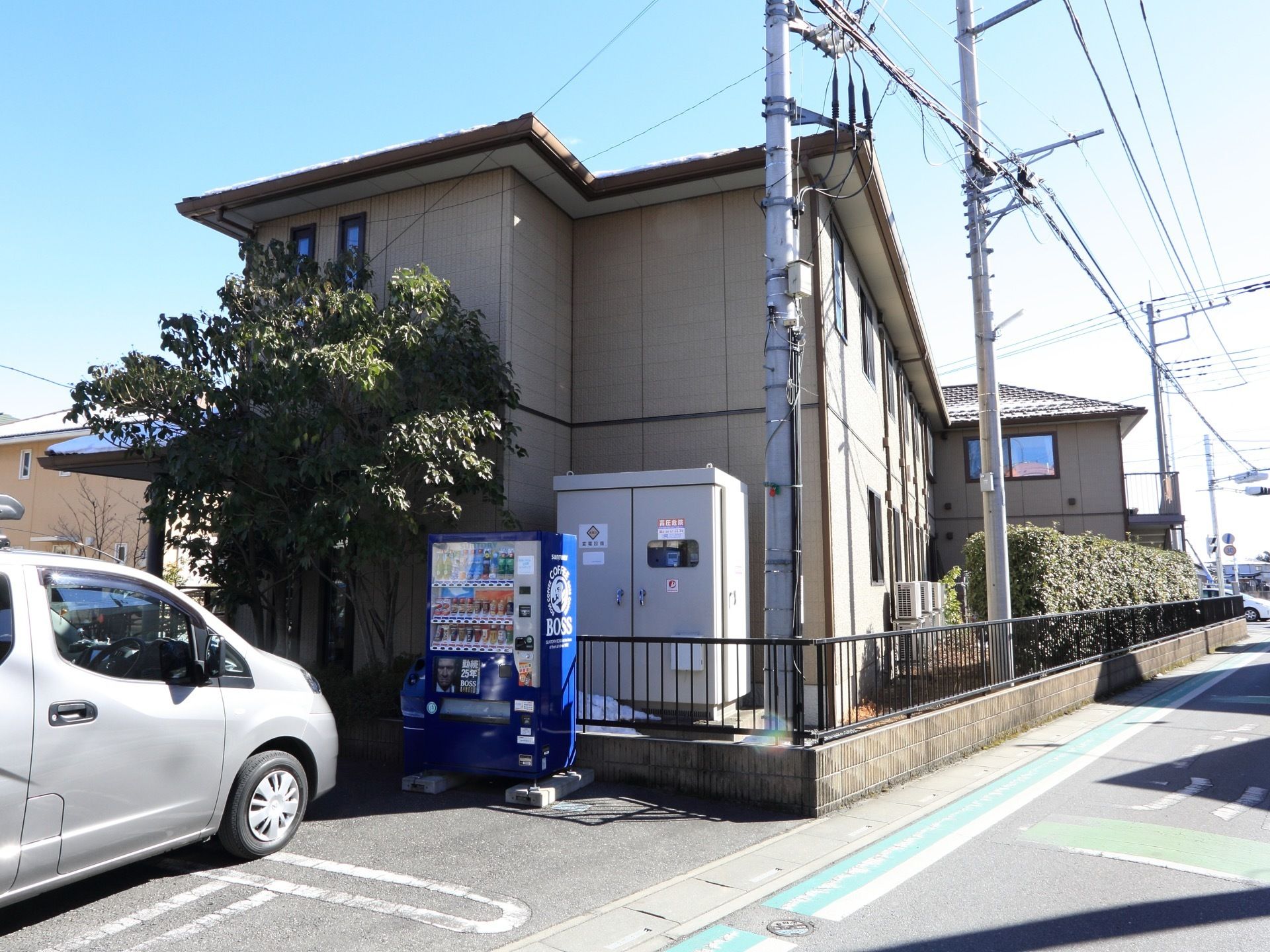 ２階建ての施設建物。ベージュを基調とし、落ち着いた印象の建物。施設の近くには飲み物の自動販売機がある。
