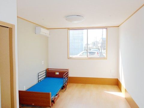 フローリング材の床と真っ白な壁が清潔感を感じさせる。介護用ベッドが壁際に置かれ、天井にエアコンが完備されている。