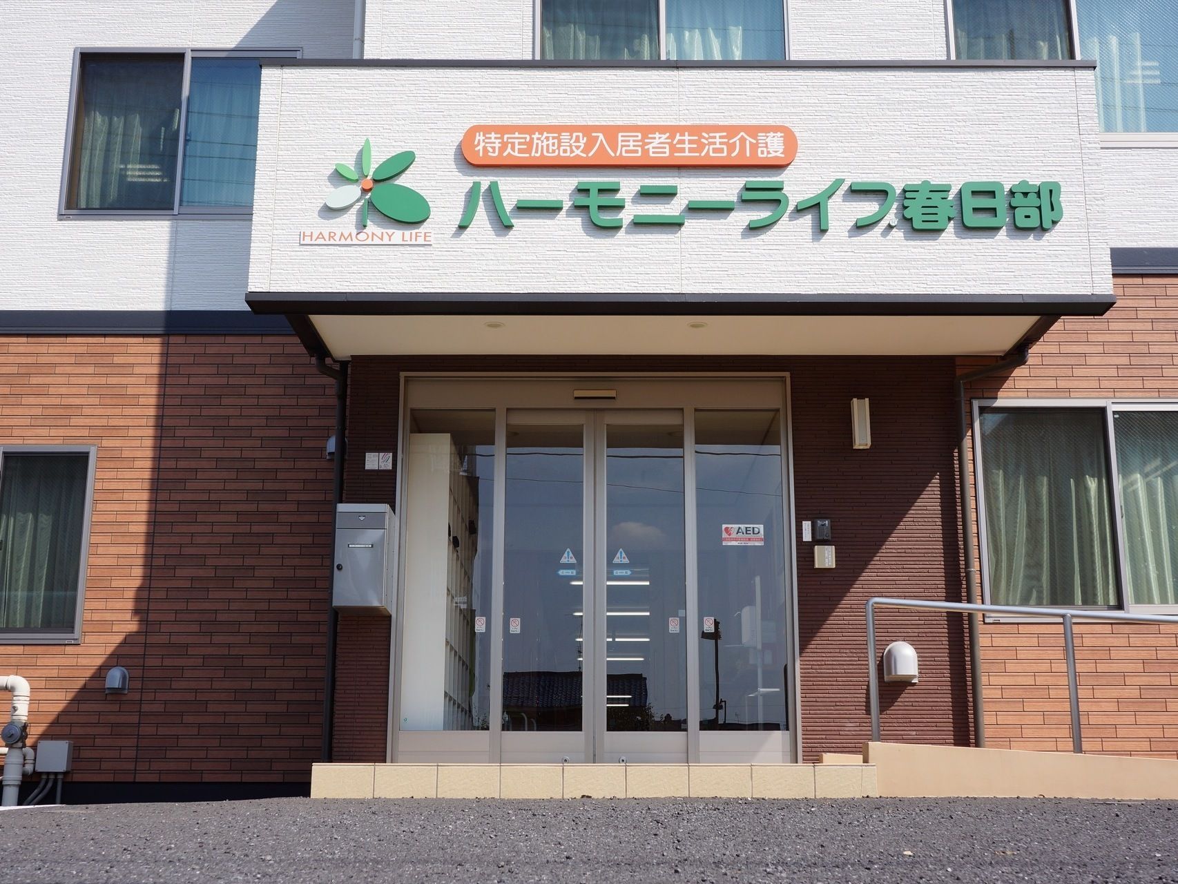 施設入口部分、自動ドアのあるエリアの上部には大きく目立つ形でシンボルマークや施設名が表記された看板が掲げられている。