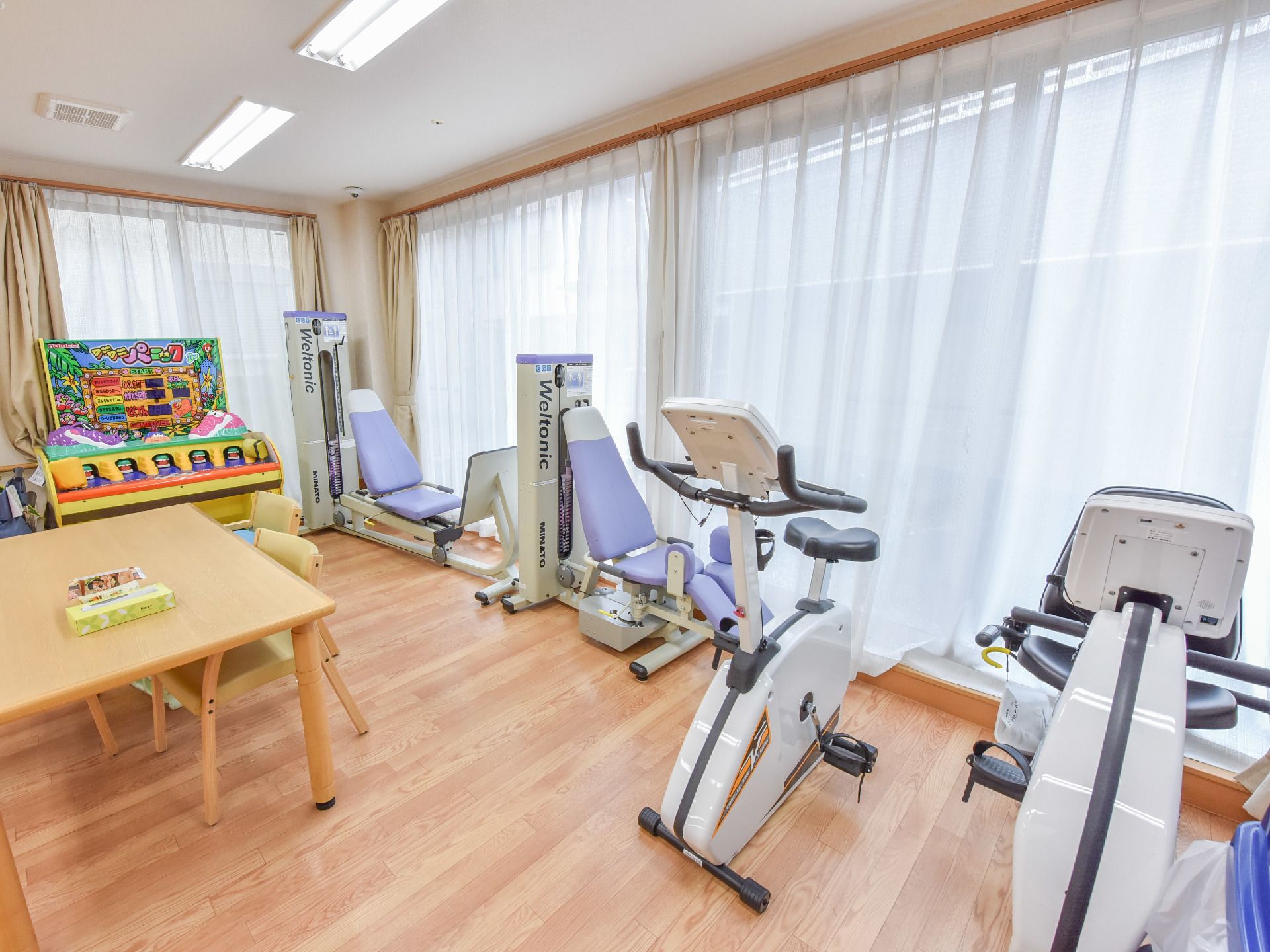 機能訓練室にはベージュ色のカーテンがかかった大きな窓があり、トレーニングマシンが4機並べられている。