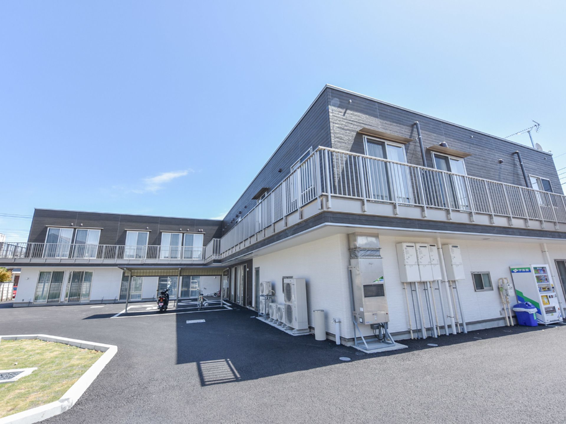 二階建ての建物。二階にはベランダがある。施設前には駐車場、庇のあるバイク、自転車用置き場が完備している。