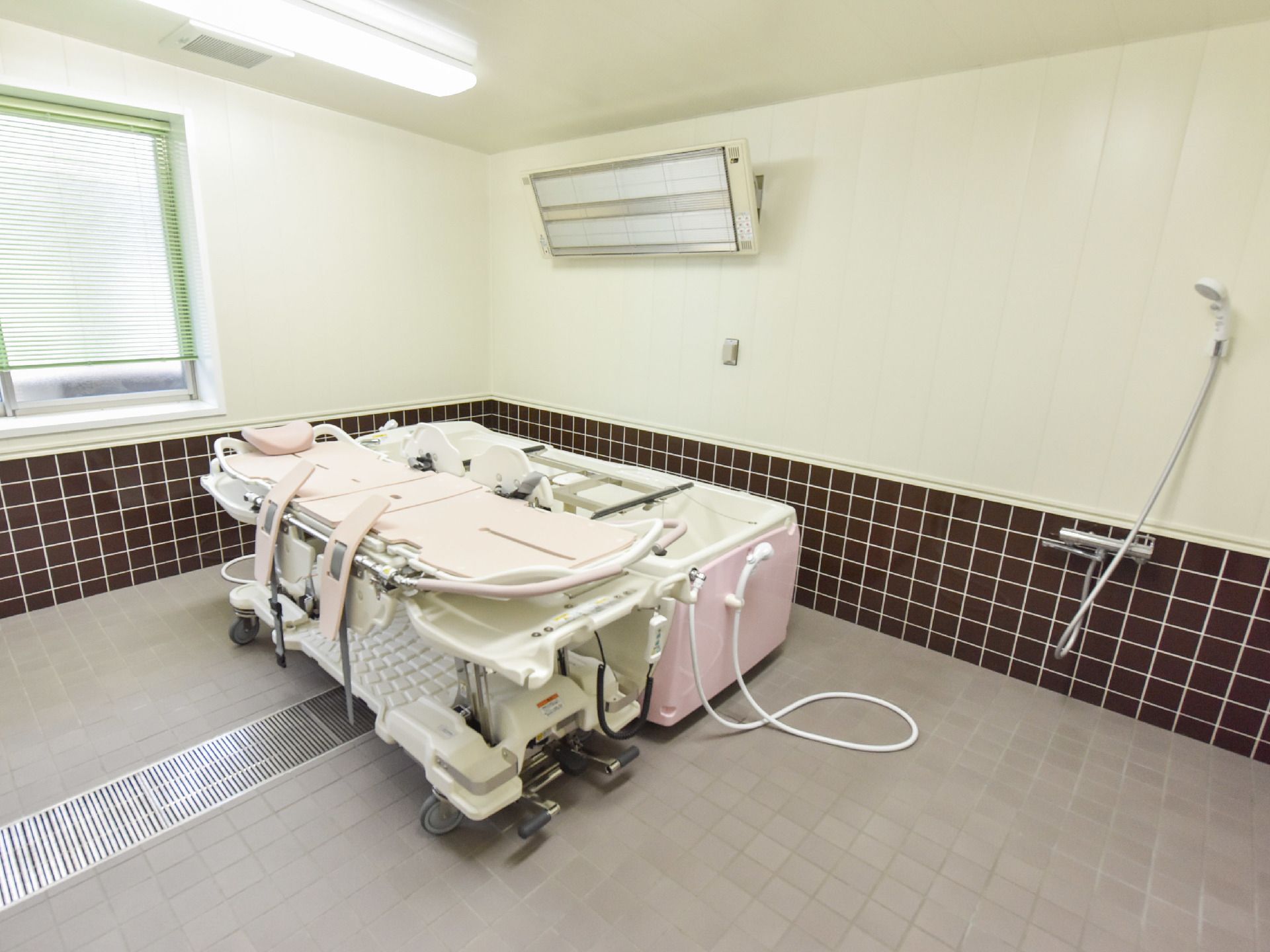 介護用の浴槽が浴室中央部にある。浴槽の周りを人が囲んでも十分余裕がある広さになっている。タイルの床に中央部に蓋付きの排水溝がある。