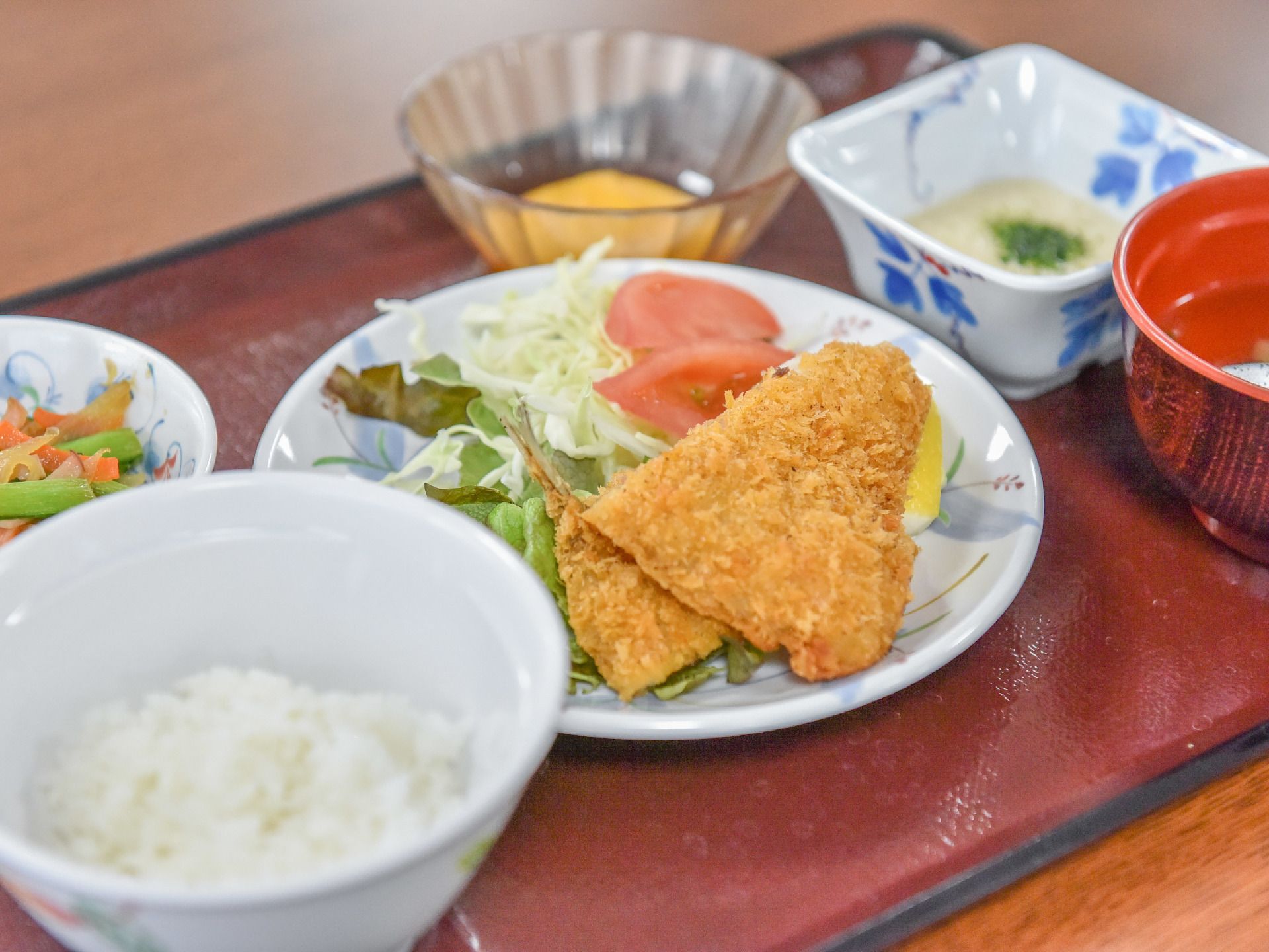 お盆の上に左手前に小盛のご飯、中央にメインのおかずのアップ、右にお椀がある。メインの奥に和え物、小鉢が二つある。