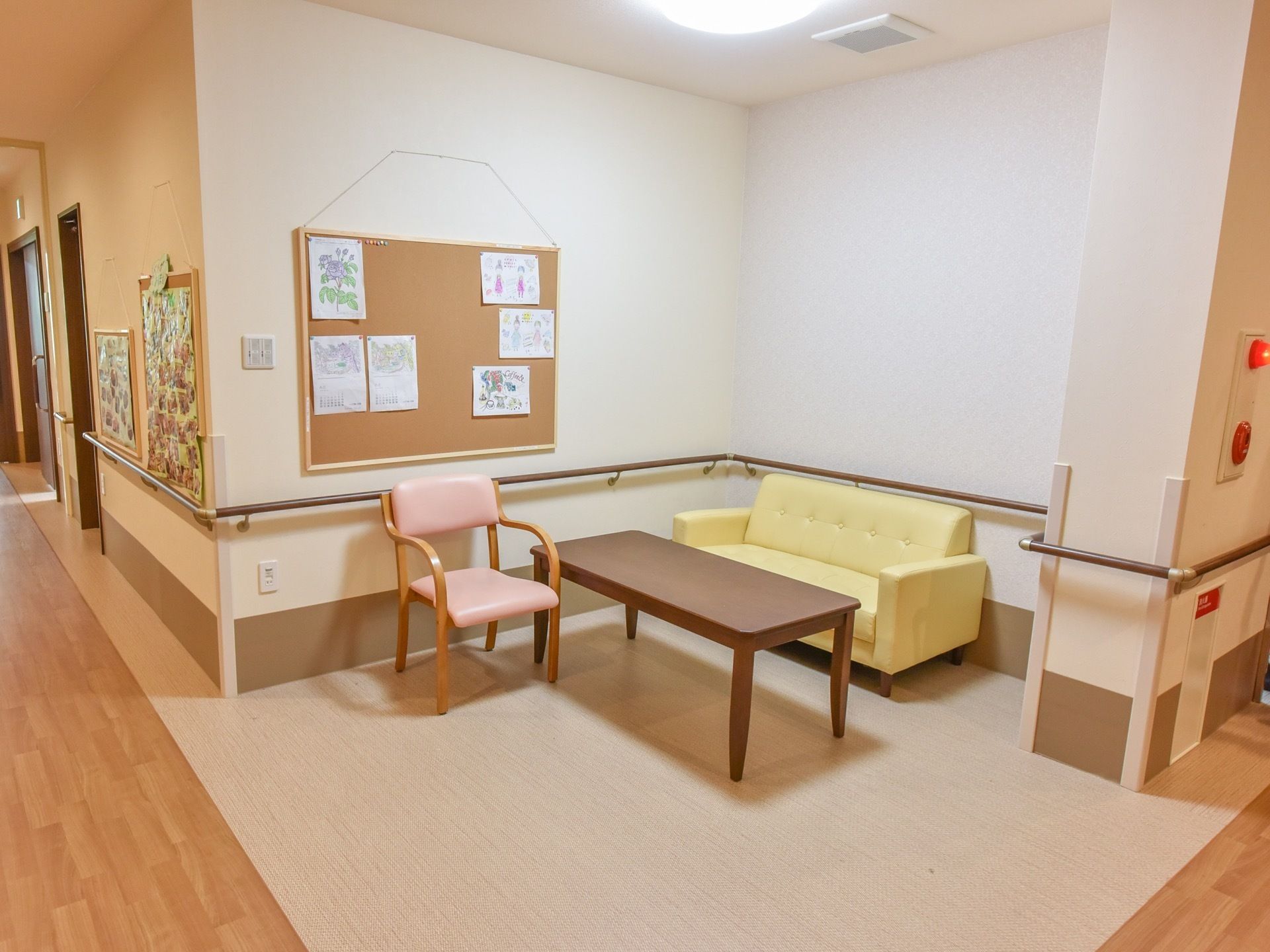 廊下には途中で休めるように椅子とテーブルが配置されている。白壁には大きなボードが吊られており、入居者様の作品が飾られている。