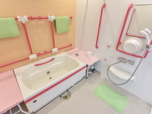 赤い手すりがたくさん付いた一人用の浴槽が設置された浴室。ベンチも付いている。