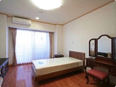 大きなガラス引き戸があり、床はフローリングになっている。ベッド、収納家具、ドレッサーが置かれ、壁と天井の色は白色基調になっている。