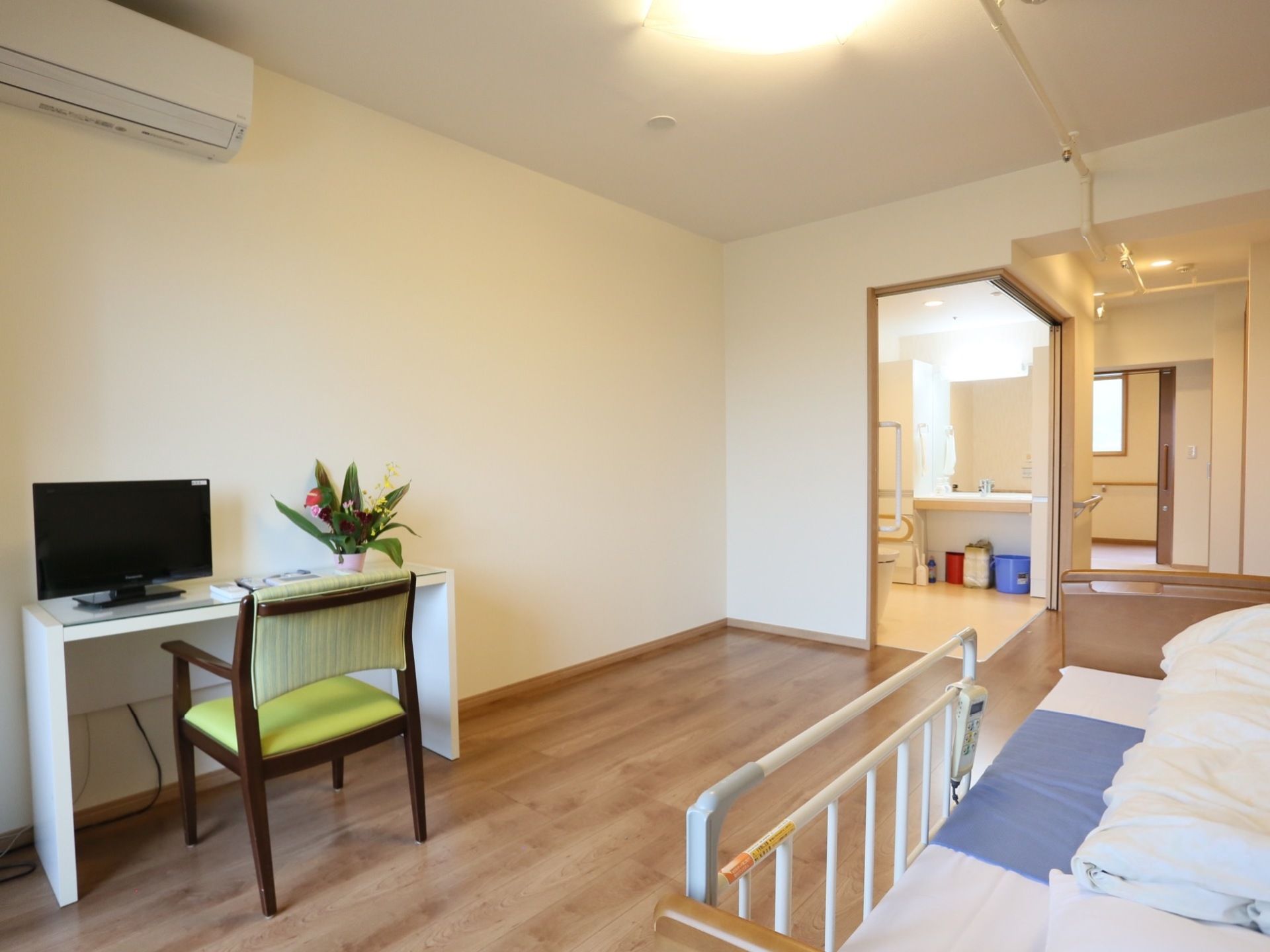 介護用ベッド、エアコン、テレビが備えつけられている。洗面所とトイレはL字型に大きく開閉できるスライド式扉となっている。