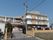 3階建ての建物が正面奥に建っている。手前には開いている黒色の門があり、その上には施設名が掲げられている。