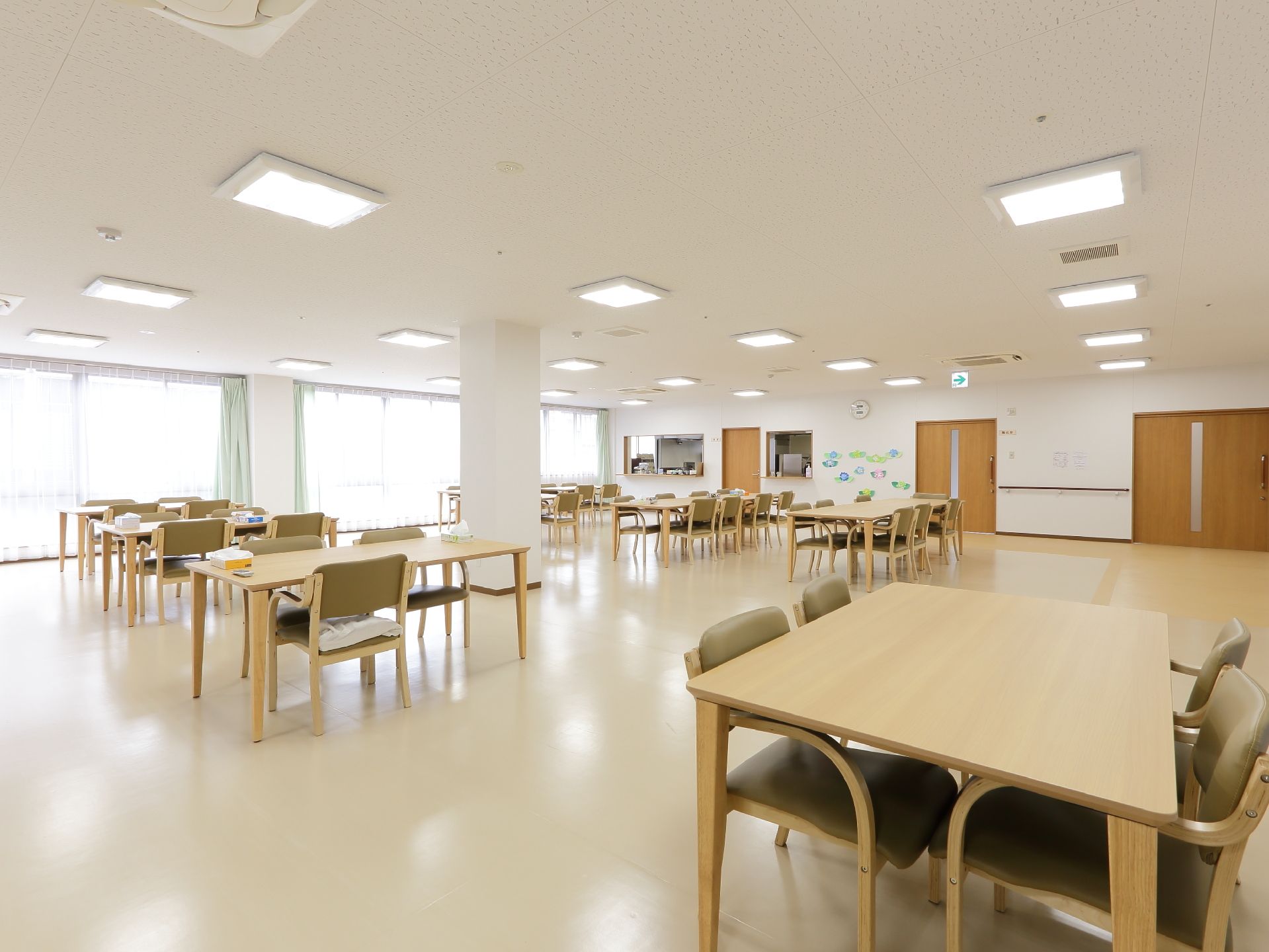 共有スペースの床は全面フラットで、ベージュ系の濃淡で一部色分けがされている。同系色のテーブルセットが複数並んでいる。