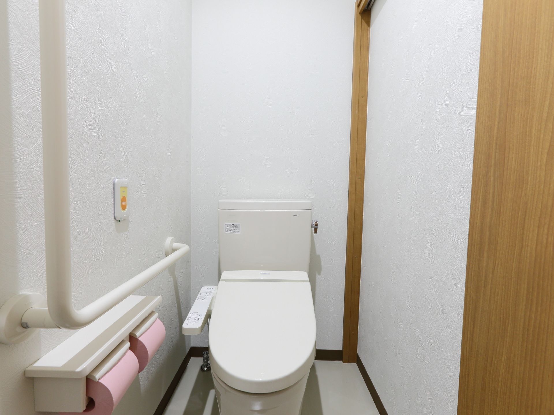 トイレの入り口ドアは木製の引き戸である。壁はエンボス模様のある白で、同色の手すりが設置されている。ナースコールがある。