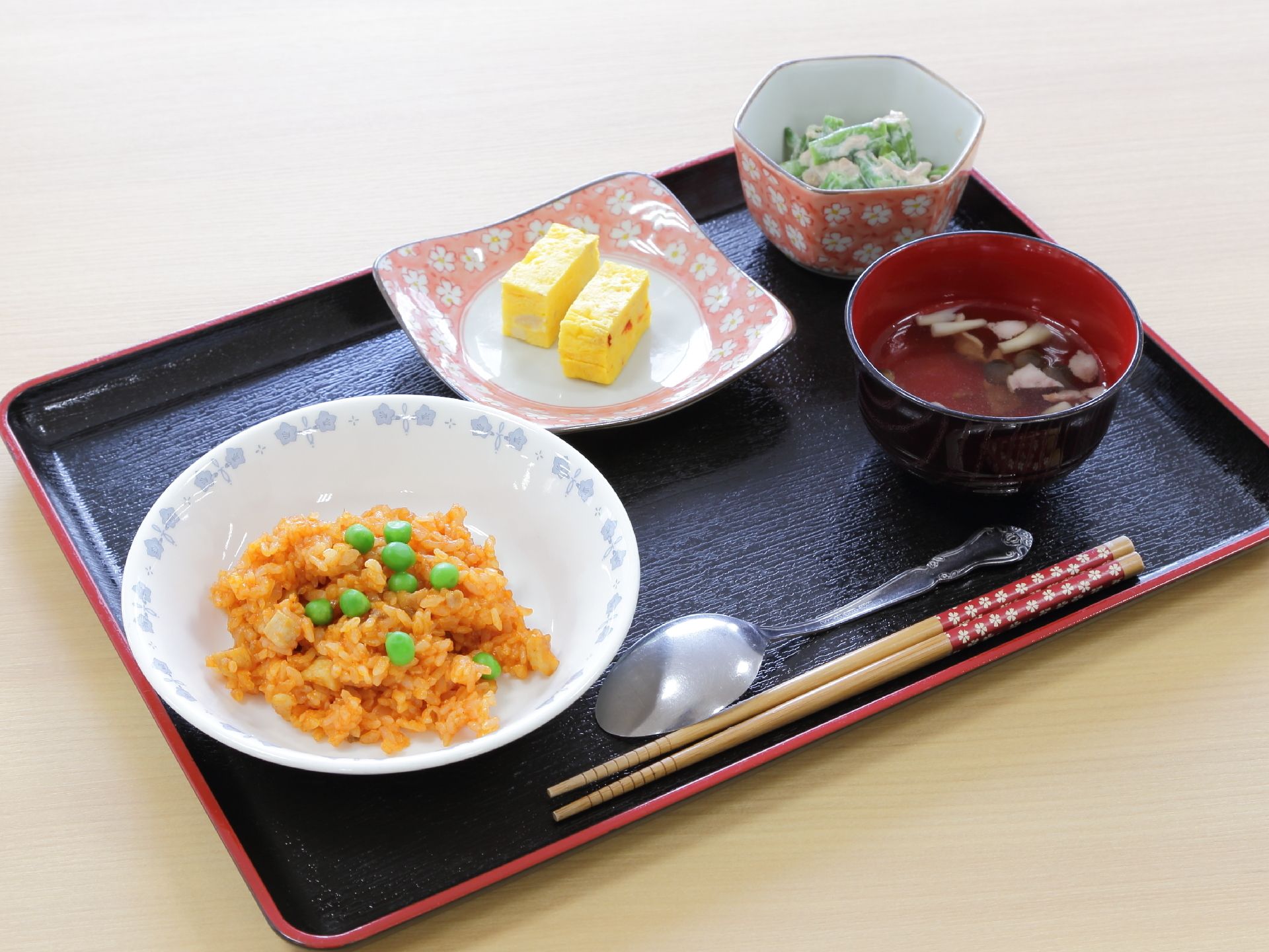 1人分の食事が長方形のトレーの上にセットされている。チキンライス、お吸い物、厚焼き玉子、野菜の和え物が並んでいる。