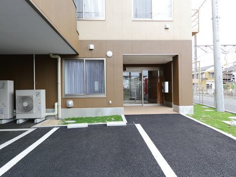 施設の入り口付近の地面はアスファルト舗装されており、左側には白いラインで区切った駐車スペースが設けられている。