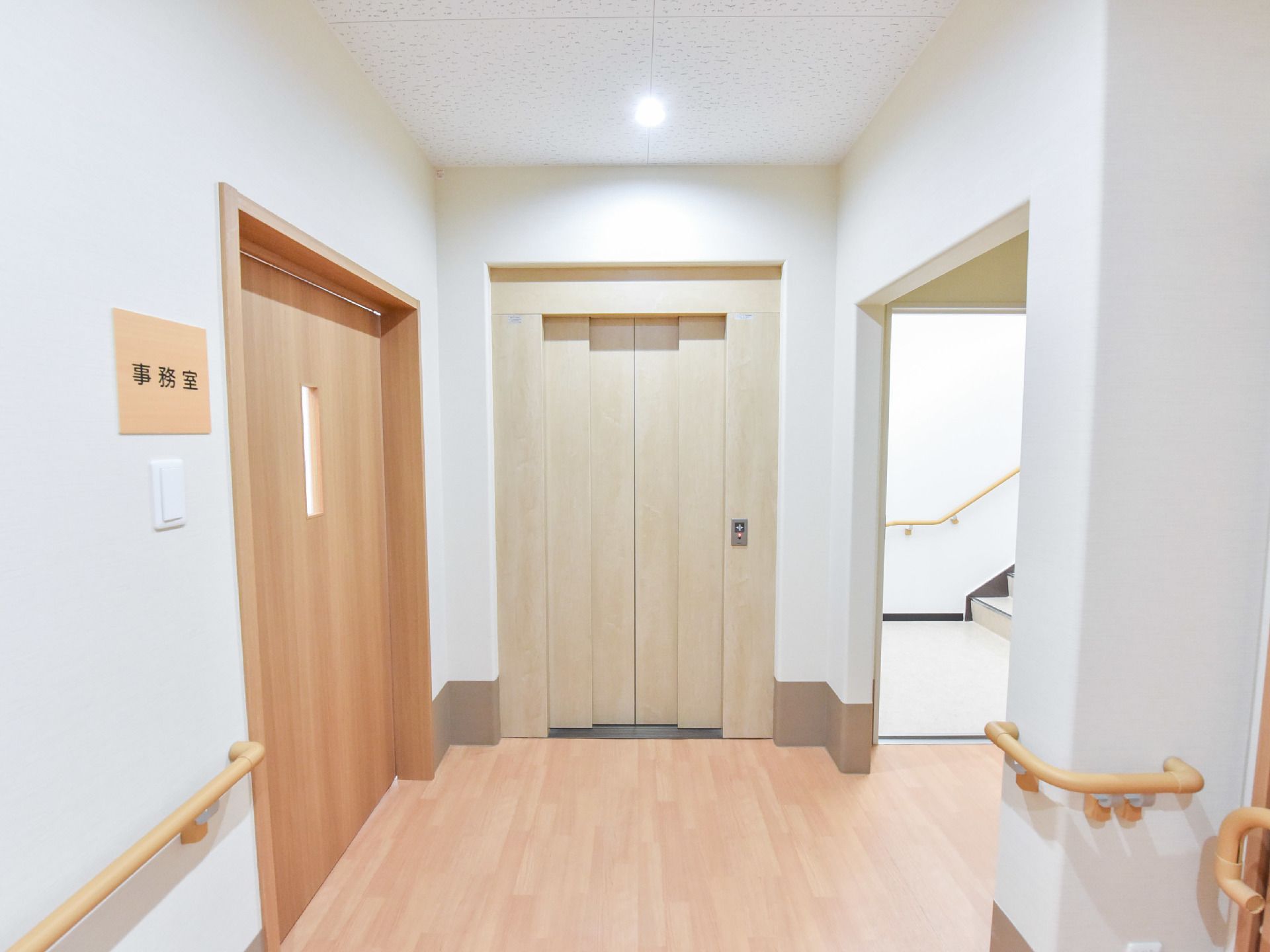 エレベーターの横には階段があり、階段にも手すりが備え付けられている。また、事務室の横側にも手すりが備え付けられている。