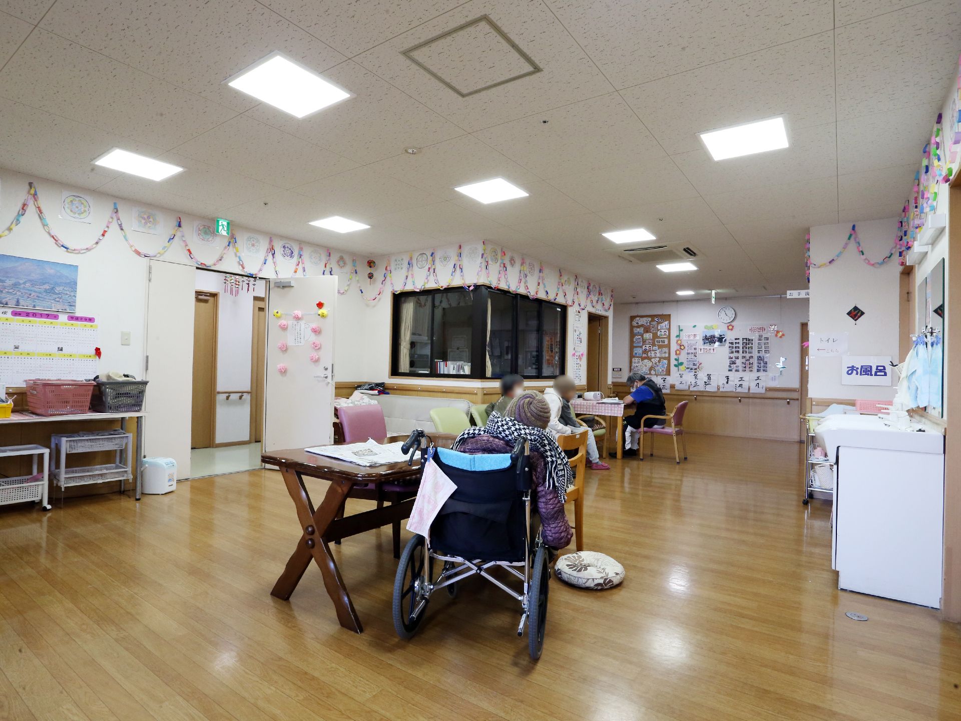 照明の光が木目調のフローリングと白基調の壁面から構成されているフロア内を明るく照らしている。壁面は色とりどりの紙細工で装飾されている。