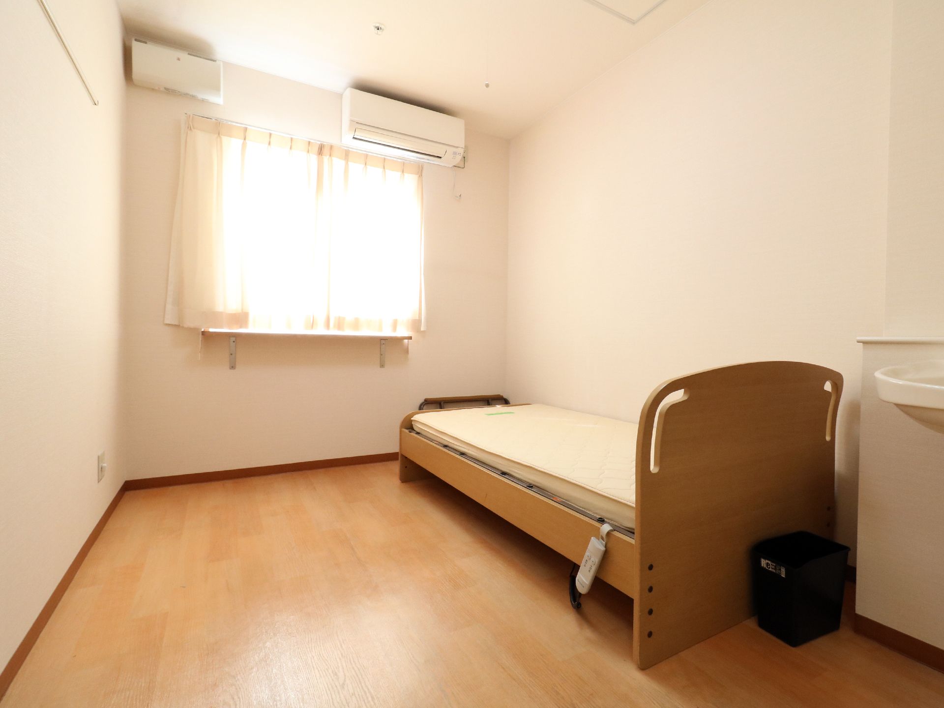 白い壁紙とライトブラウンの床が落ち着いた雰囲気の部屋である。バリアフリー仕様の床で安全。壁にはエアコンも付いている。