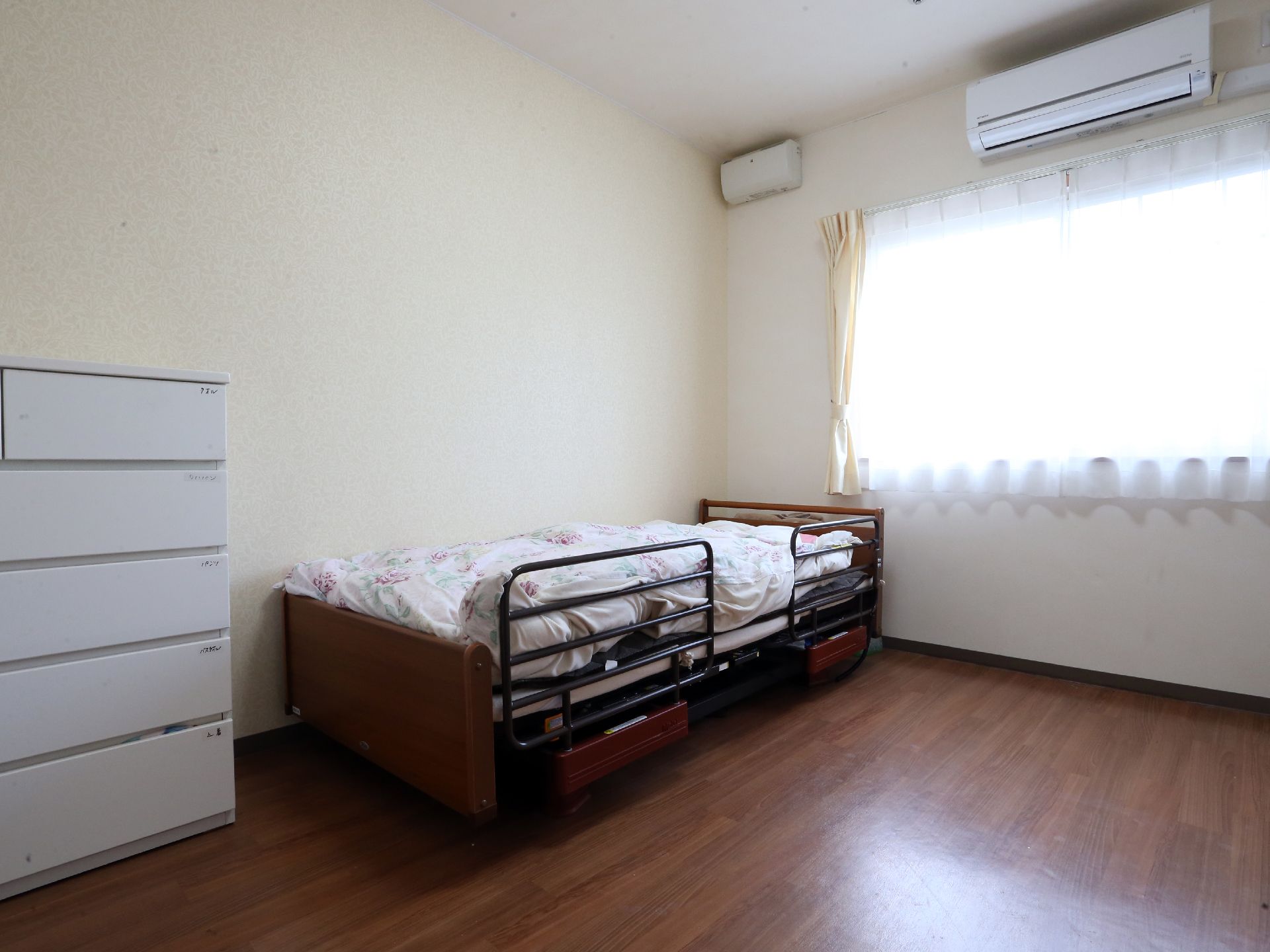 白い壁が明るく爽やかな雰囲気の部屋である。バリアフリー仕様の床で安心。壁にはエアコンも設置されている。