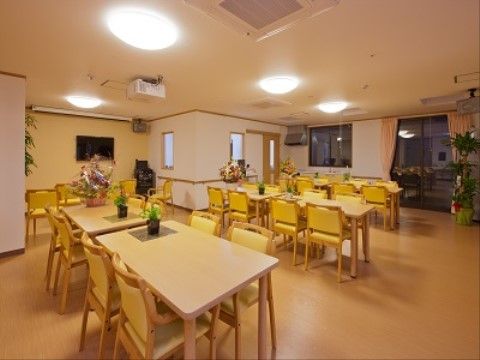 広々としたスペースに木の色のテーブルや黄色い椅子を余裕を持って配置したリビングでは、リラックスした環境で入居者様にお食事していただける。