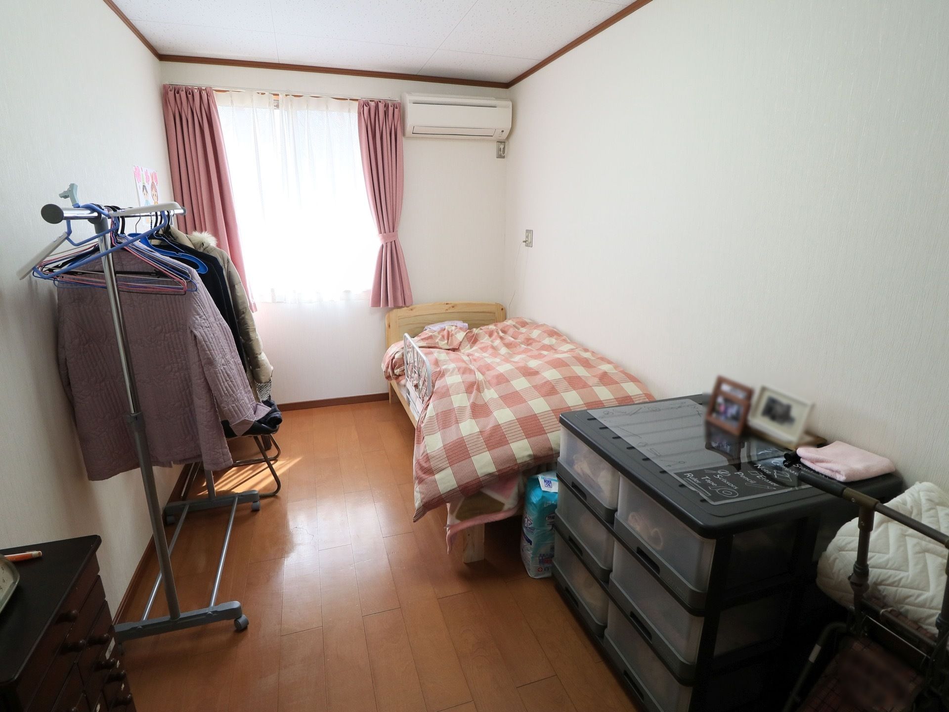 個室タイプの部屋になっている。窓はピンク色のカーテンが掛けられている。床はフローリングになっている。綺麗に整理整頓されている。