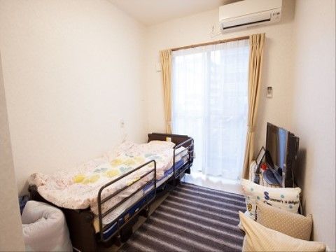 じゅうたんが敷かれた部屋にベッドが置かれている。ベッドはこげ茶色で、転倒防止用の柵が設置されている。