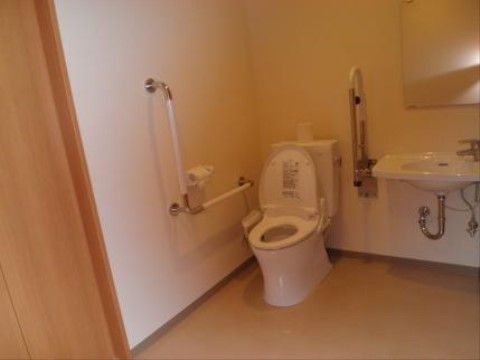 広い居室のトイレは、便座の両サイドに手すりを完備しているので、立ち座りの動作も安心である。隣の洗面で手洗いもでき清潔である。