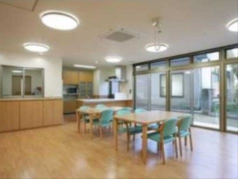 壁一面が窓で、隣の建物や植木がよく見える。窓の近くにテーブルが２つ並べて置いてあり、緑色の椅子が用意されている。