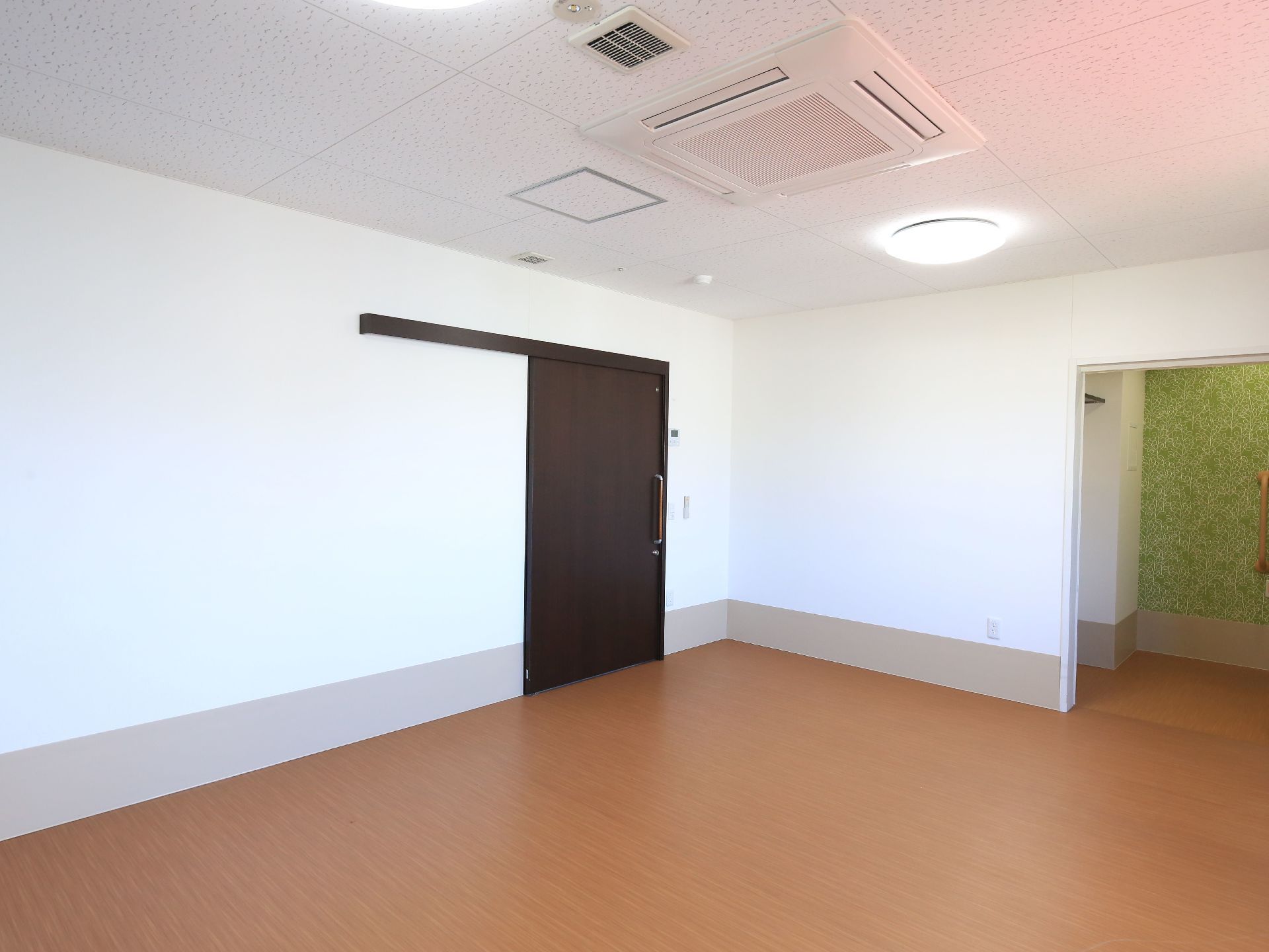 二人部屋は広く、家具類を設置してもゆったりと生活できるようなスペースを確保している。天井エアコンが取りつけられている。