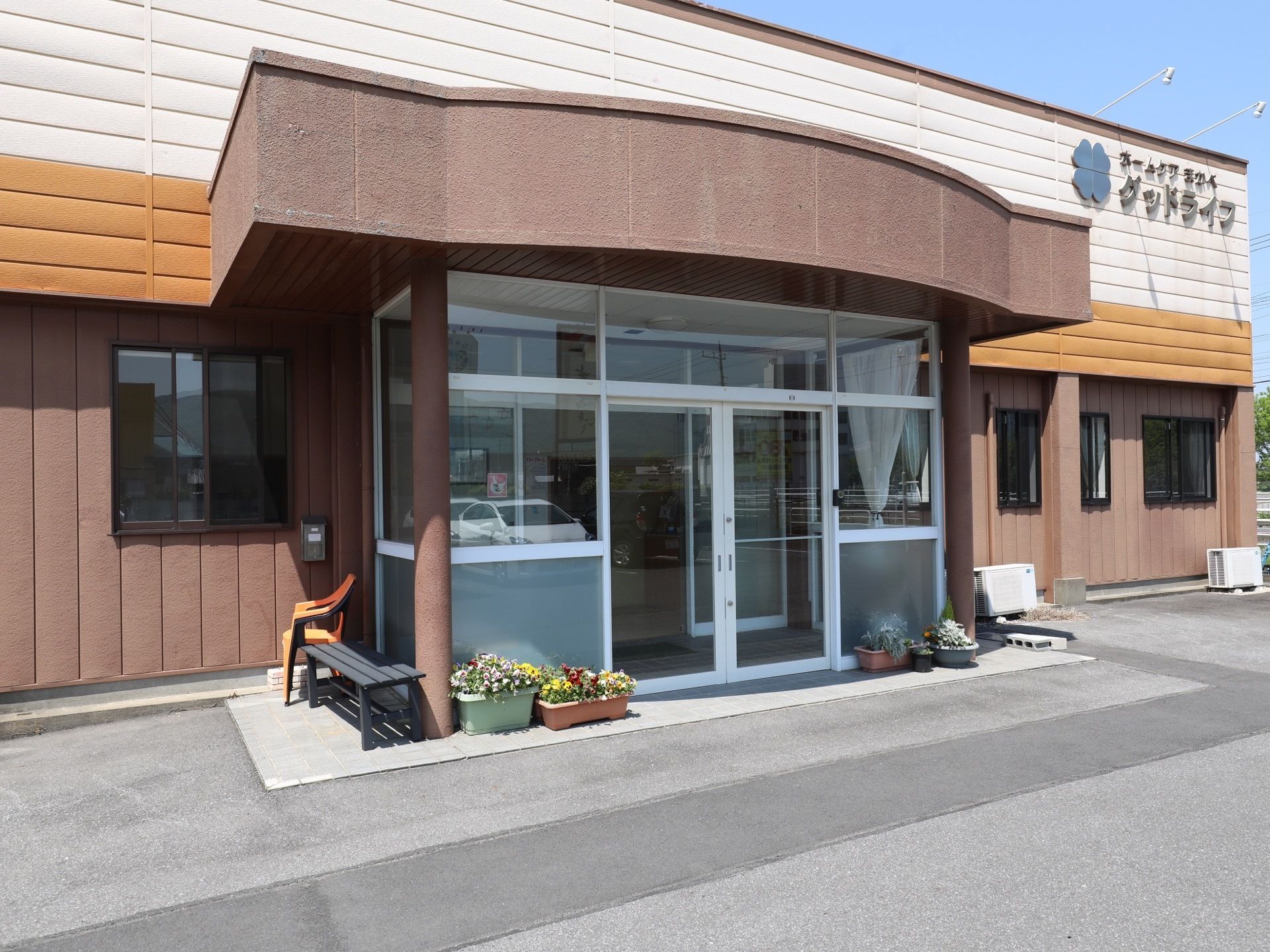 屋根付きのガラス張りのドアの目の前には、手入れの行き届いたプランターが置かれている。玄関横にはベンチが設置されている。