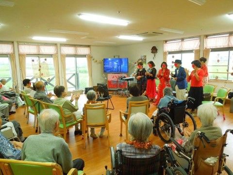 入居者様が椅子に座り、前に立つ演奏者に拍手を送っている様子