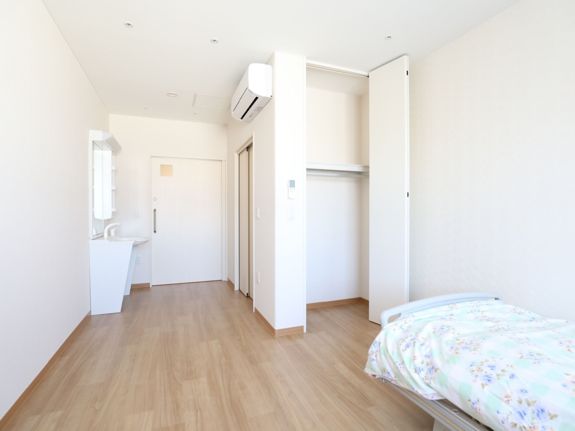 木目調の床と白い壁面で構成された居室である。出入口は引き戸である。手洗いスペースがある。エアコンが設置されている。