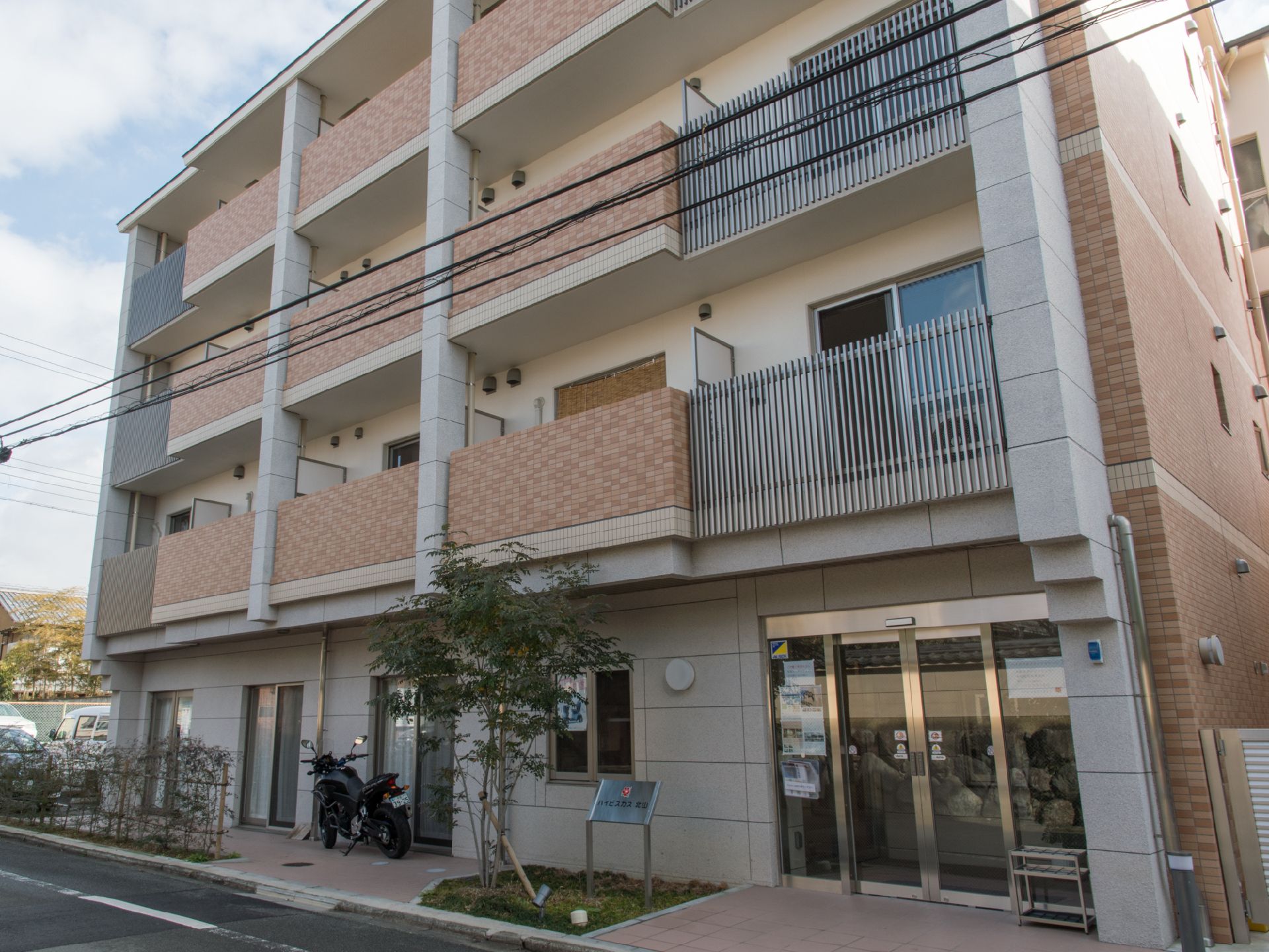 建物の外観からは、丈が高めの外枠を設置しベランダをしっかりガードしているのが分かる。1階のエントランスはガラス張りのドアになっている。