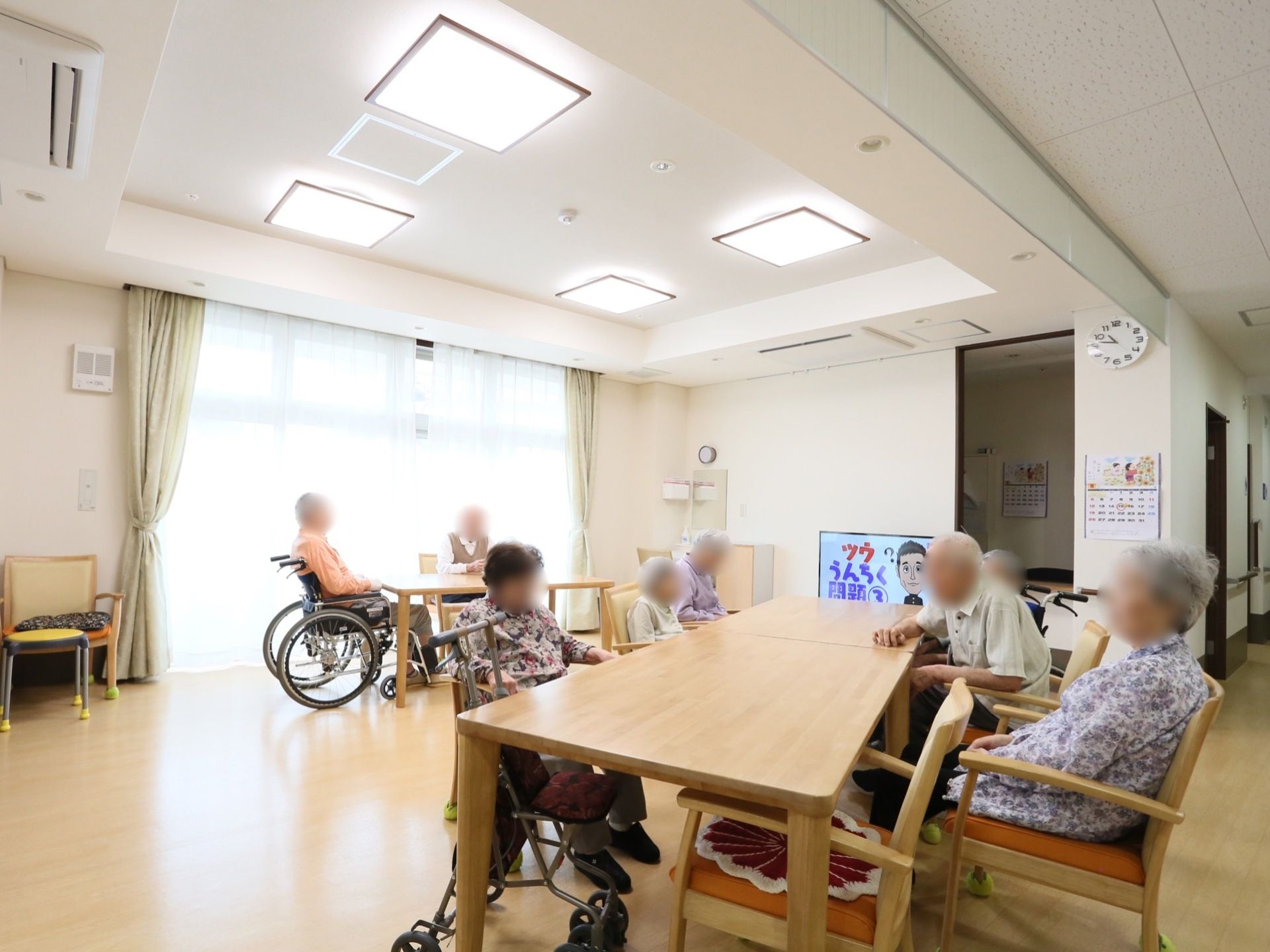 明るい色調の共有スペースである。広々としたテーブルと背もたれ椅子を完備。大きなテレビも備えつけられている。