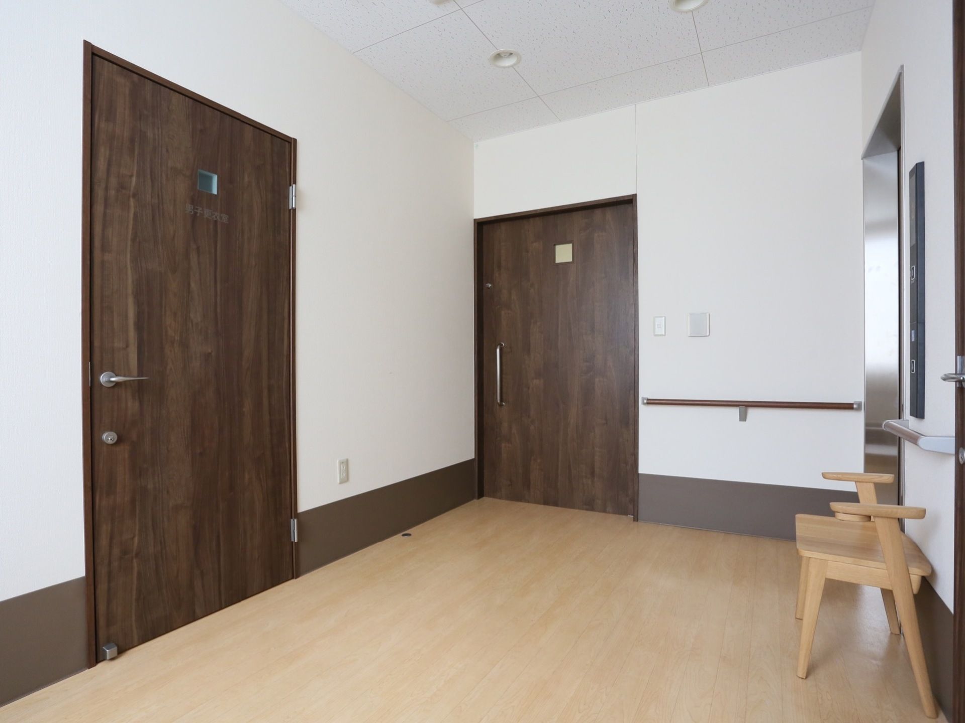 明るい床色に白い壁、扉は濃い茶色に施されている。エレベーター前はじゅうぶんな広さがある。椅子も完備。