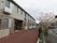 左手に建物。園路があり、右手に駐車場がある。園路は玄関までは茶色の舗装でそれより奥はアスファルト舗装である。駐車場と園路の間に桜の木がある。