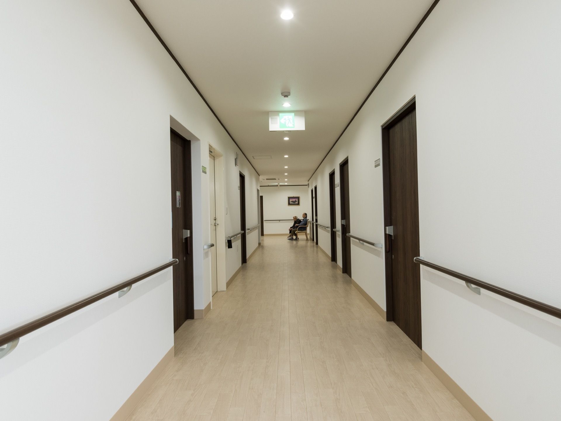 通路の幅は広く、両側に部屋の扉が並んでいる。壁には茶色い手すりが取り付けられている。椅子も置かれている、