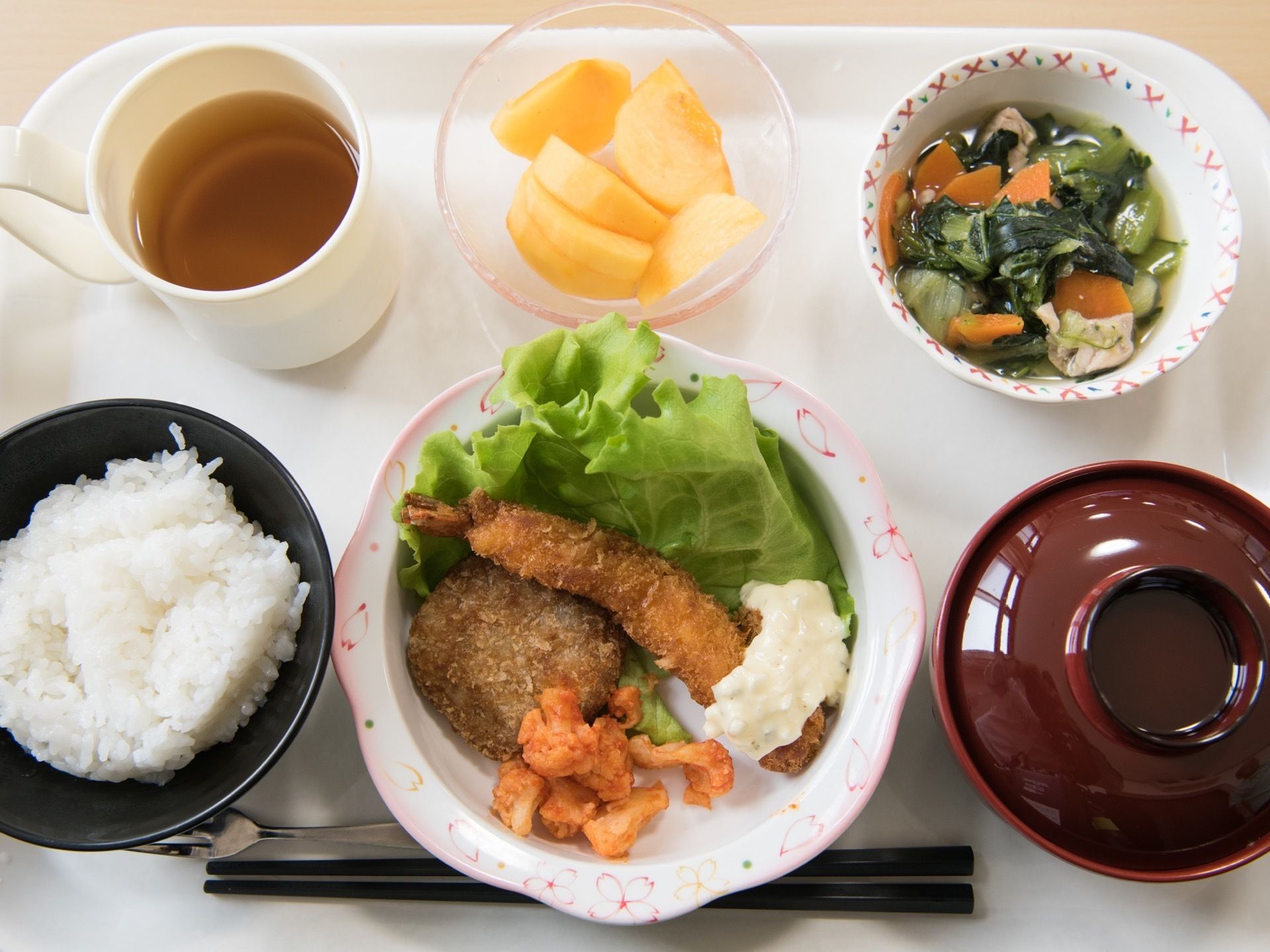 白いお盆にはご飯を含む5品のメニューが並べられている。フルーツもメニューにあり、専用のフォークも置かれている。
