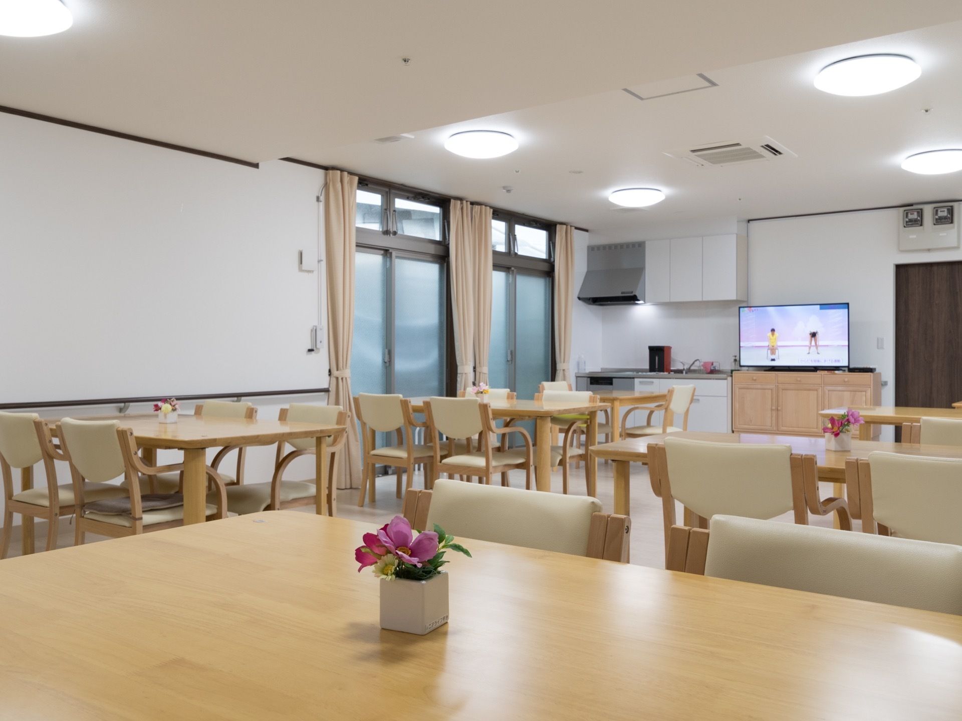食堂のキッチンスペースの横には大きな窓があり、テレビが置かれている。テーブルには小さなお花が飾られている。