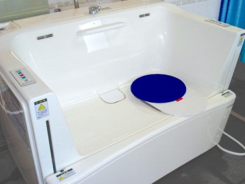 座ったままの姿勢で入浴できる機械浴槽が置かれている。清潔感のあるバスタブで、奥に青いカーテンが取り付けられている。