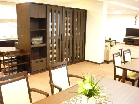 お洒落なシェルフがあり、奥にはテレビとソファーがあり、手前には机と椅子があるダイニングルーム