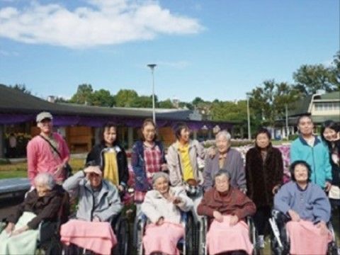 緑豊かな公園を背景に、和気あいあいと写真撮影する入居者様とスタッフの様子