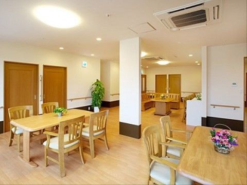 白を基調としたフローリングの床の空間である。テーブルと椅子がいくつも配置されている。各テーブルには花が飾られている。