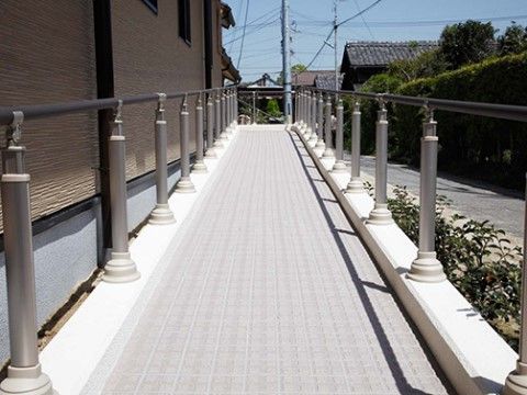灰色のタイルで舗装されたスロープが設置されている。スロープの両側には手すりが取り付けられ、道路側に植物が植えられている。