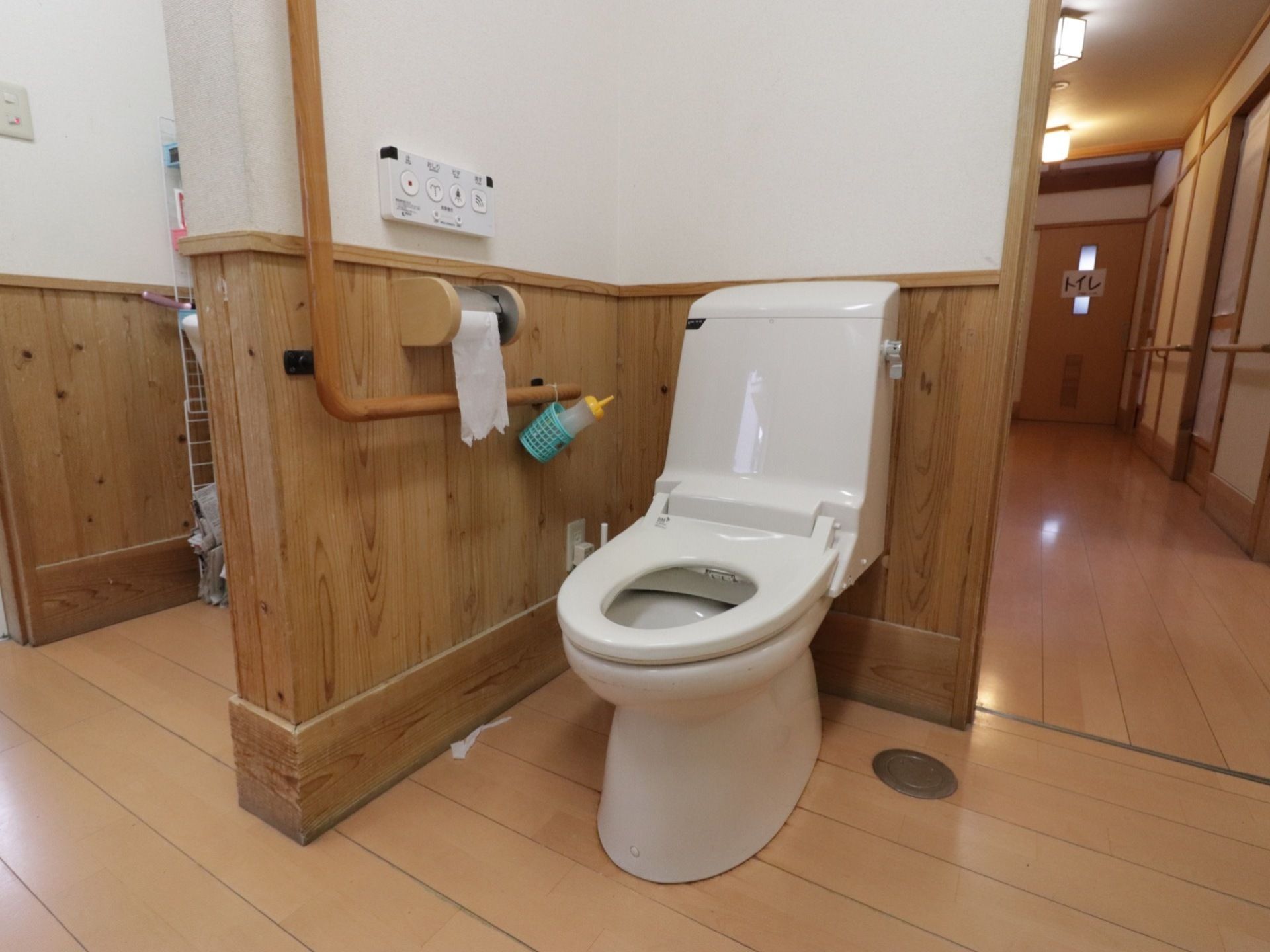 オープンスペースに設置されたトイレである。二面に壁があり、便器横の壁に手すりや温水洗浄便座のリモコンが設置されている。
