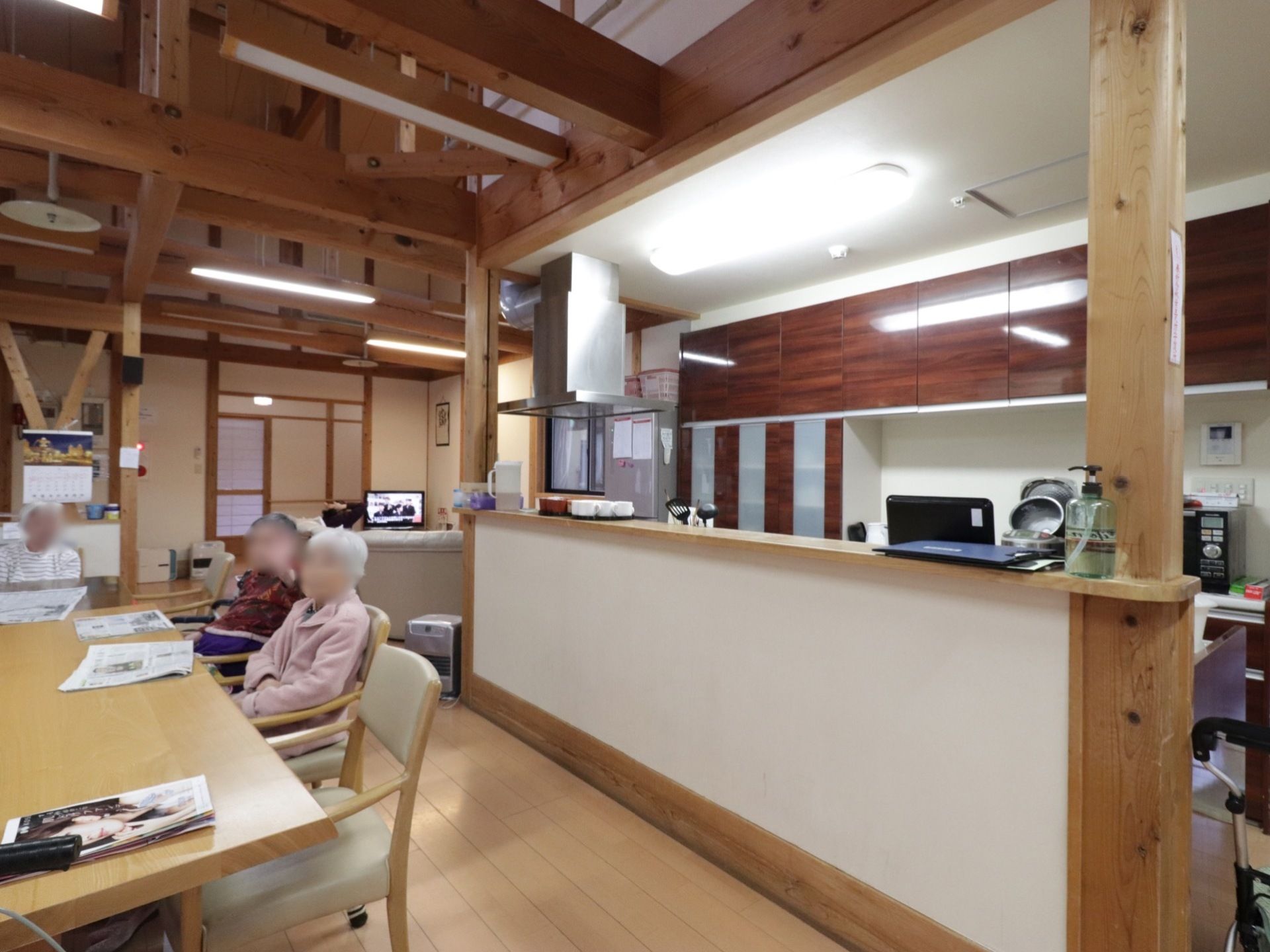 天井が高く、梁が見えるデザインの食堂である。大きなダイニングテーブルがあり、奥にテレビやソファが置かれている。